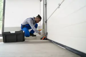 A hand applying lubricant to a garage door roller for smoother operation.